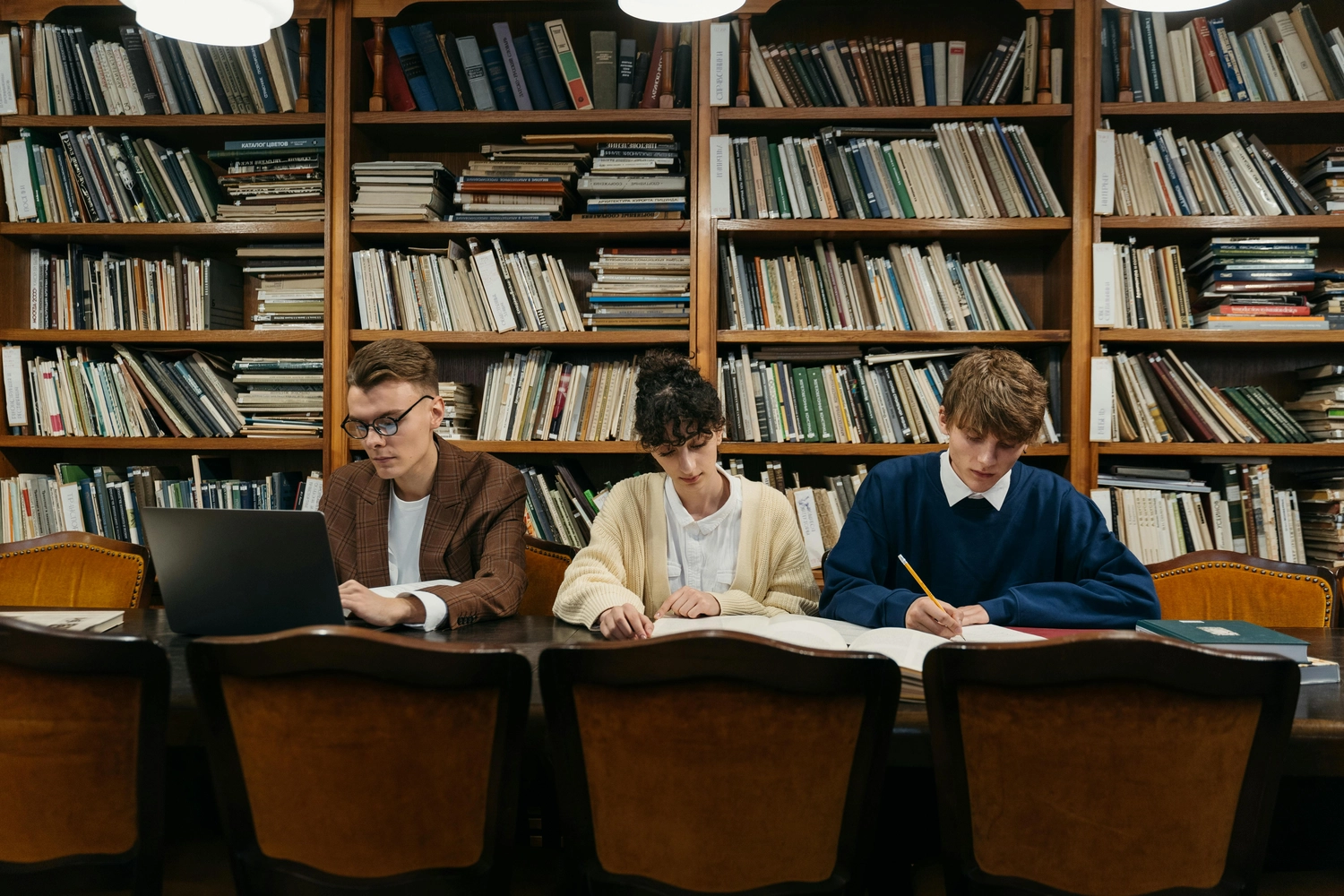 Prof. Dr. Marcus Mittenzwei - Hochschullehrer - Drei Schüler lernen an einem Bibliothekstisch vor Büchern.